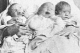 A black and white photo of three babies being held by an unseen nurse.