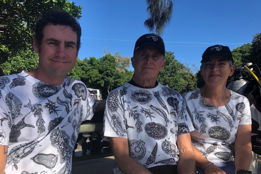 A younger man, an older man and a woman sit side by side wearing matching t-shirts wearing t-shirts featuring a nudibranch print