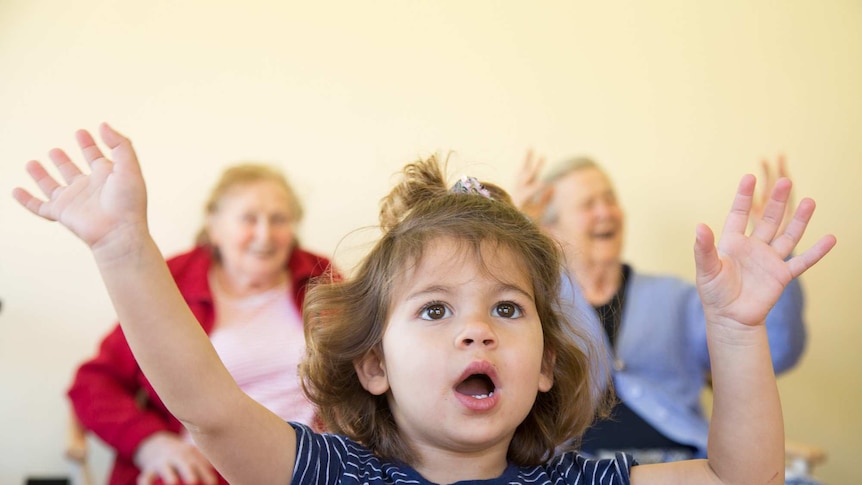 A little girl lifts her arms miming nursery rhyme Twinkle Twinkle Little Star as residents do the same behind her