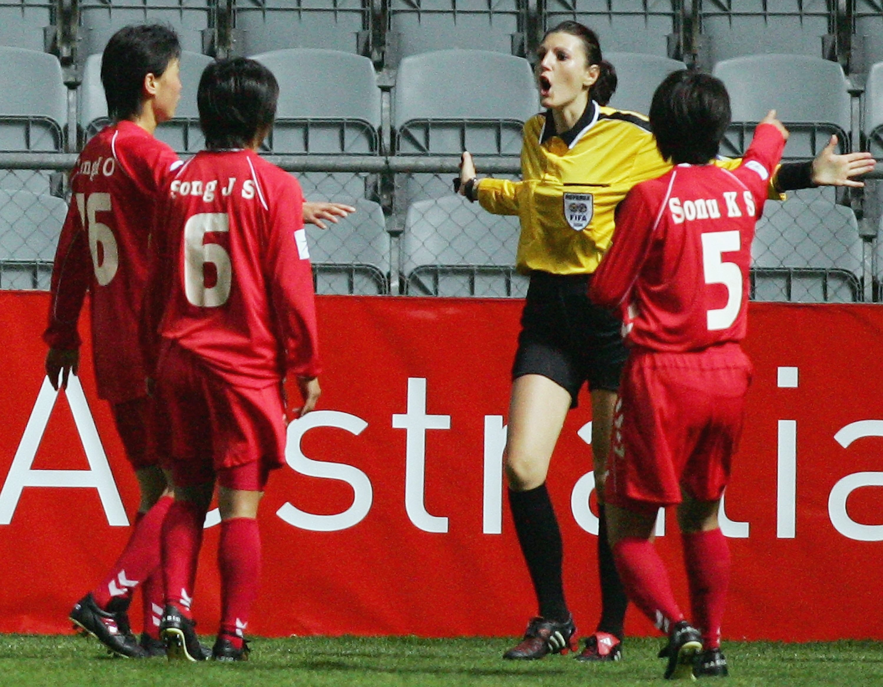 Soccer players wearing red and white argue with a woman wearing yellow and black during a sports match