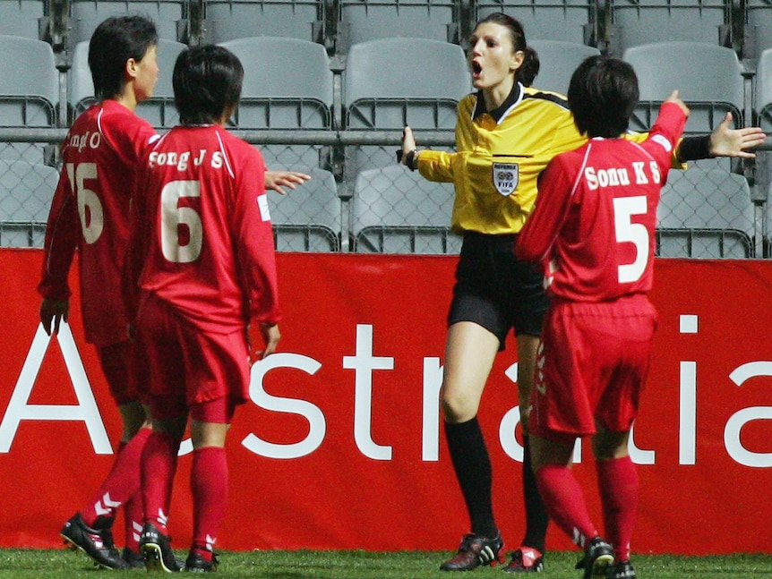 Soccer players wearing red and white argue with a woman wearing yellow and black during a sports match