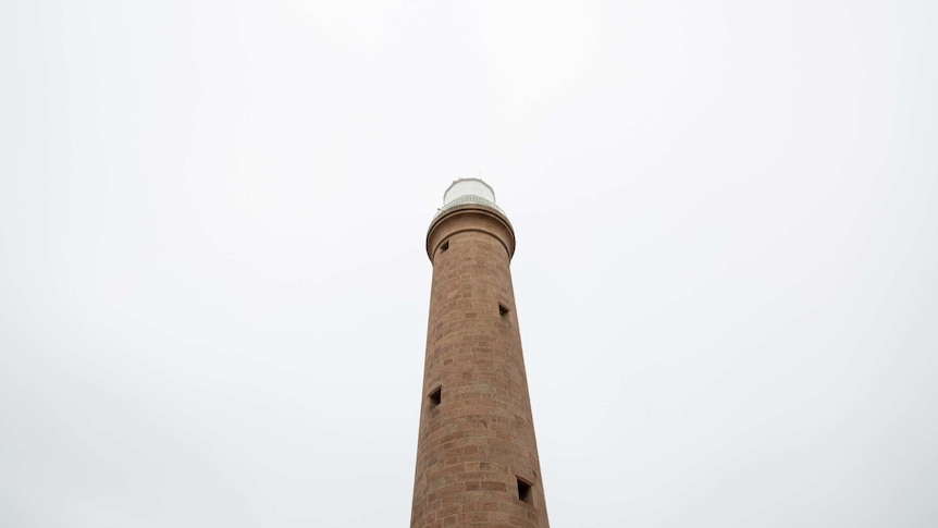 The lighthouse tower is seen from below against an expanse of white sky.