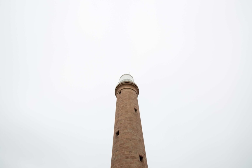 The lighthouse tower is seen from below against an expanse of white sky.