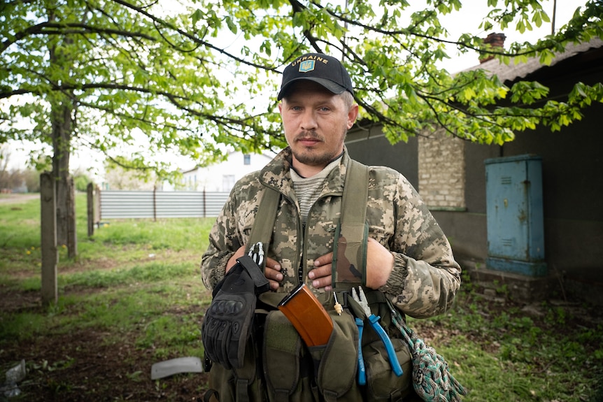 A man wearing military gear stands in the frontyard of a house.