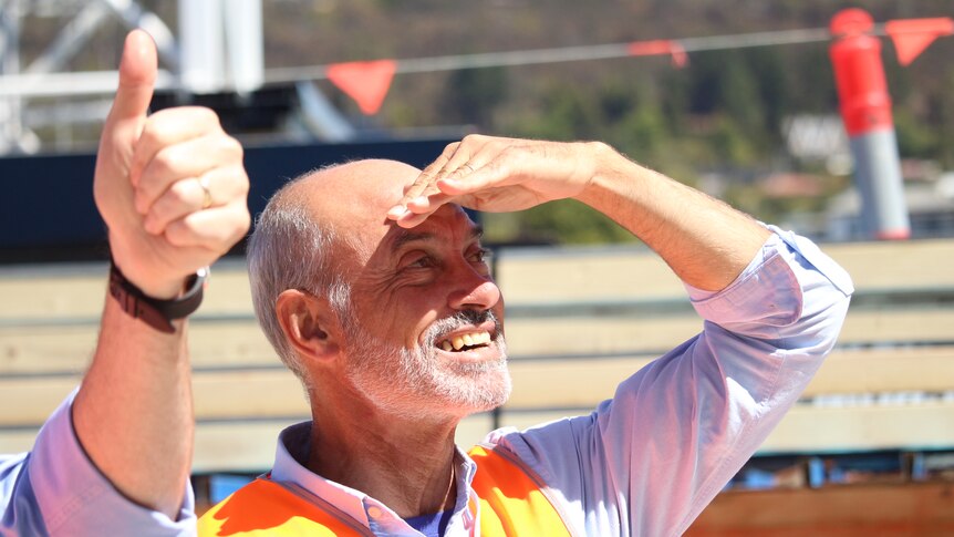 A man shields his eyes from the sun, while someone else gives the thumbs up
