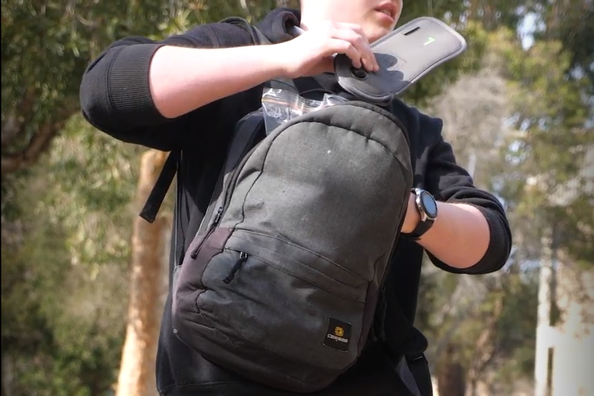 School student in black uniform pulls yondr phone pouch out of their black back pack