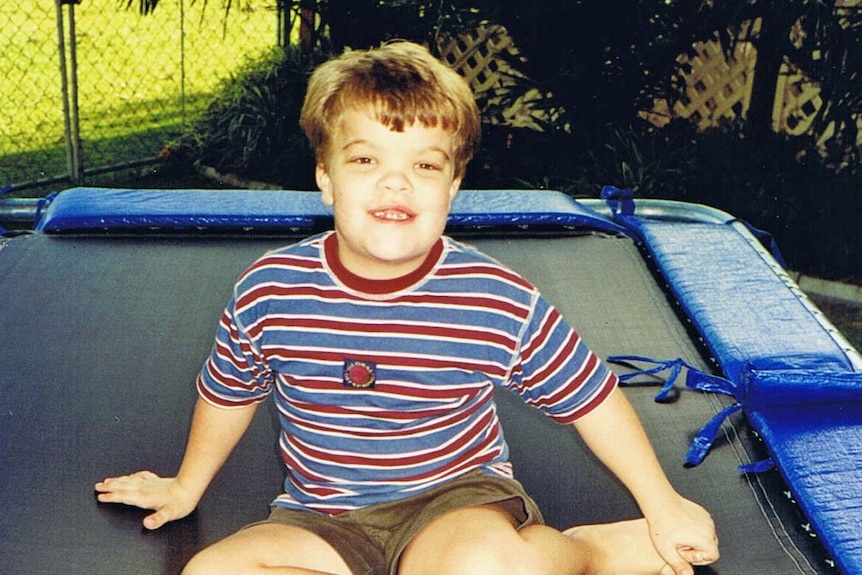 a young boy in a striped t-shirt sitting on a trampoline