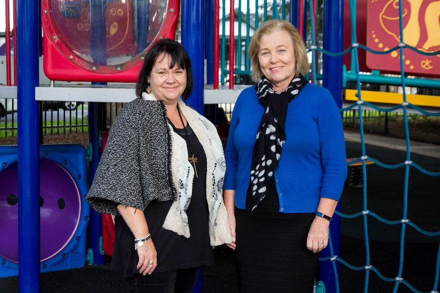 Two women stand next to playing equipment.