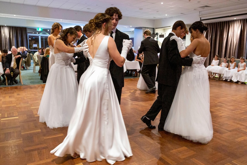 Boys and girls dance together on a dance floor surrounded by people sitting at tables.