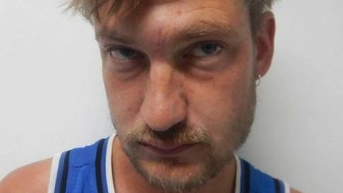 Police profile picture of white man with short, sandy hair and facial hair. He wears a blue singlet and has glassy eyes