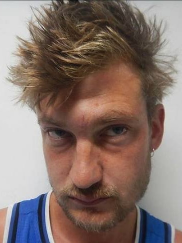 Police profile picture of white man with short, sandy hair and facial hair. He wears a blue singlet and has glassy eyes