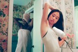 Woman blow-drying her armpit hair in front of the bathroom mirror