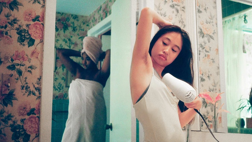 Woman blow-drying her armpit hair in front of the bathroom mirror