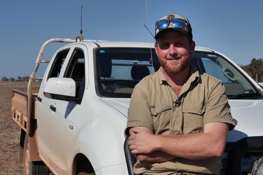 A farmer stands in front of his ute, smiling