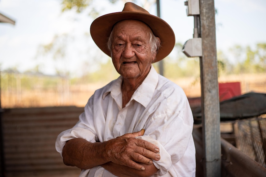 A portrait of 90-year-old former stockmen Bill Harney sitting with arms crossed, mouth open, wearing a brown hat