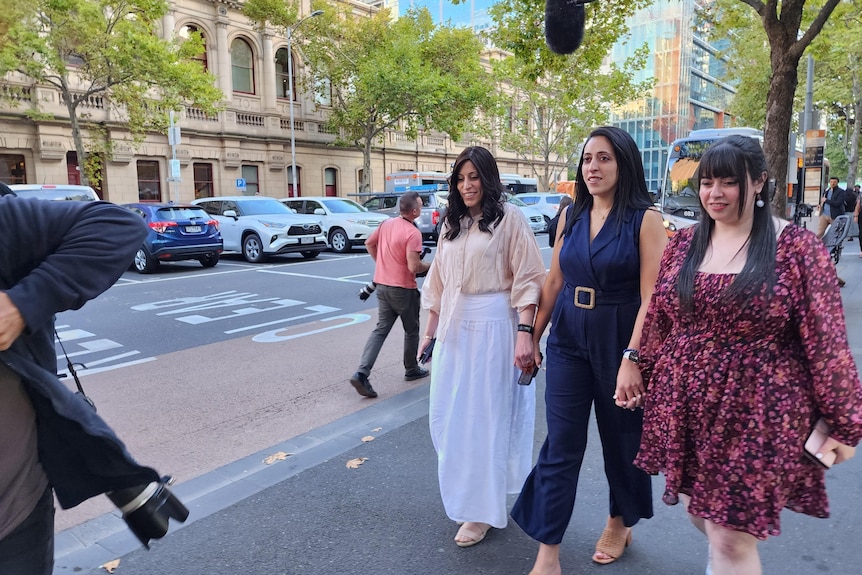 Nicole Meyer, Elly Sapper and Dassi Erlich hold hands as they walk down a street in the law precinct of Melbourne's CBD.