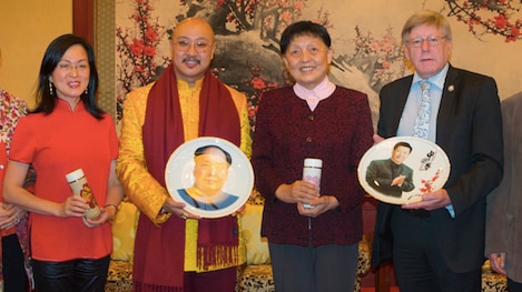 Woman in red, man in gold and red scarf holding plate, man in burgundy cardigan and man in suit and tie holding ornamental plate