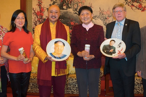 Woman in red, man in gold and red scarf holding plate, man in burgundy cardigan and man in suit and tie holding ornamental plate