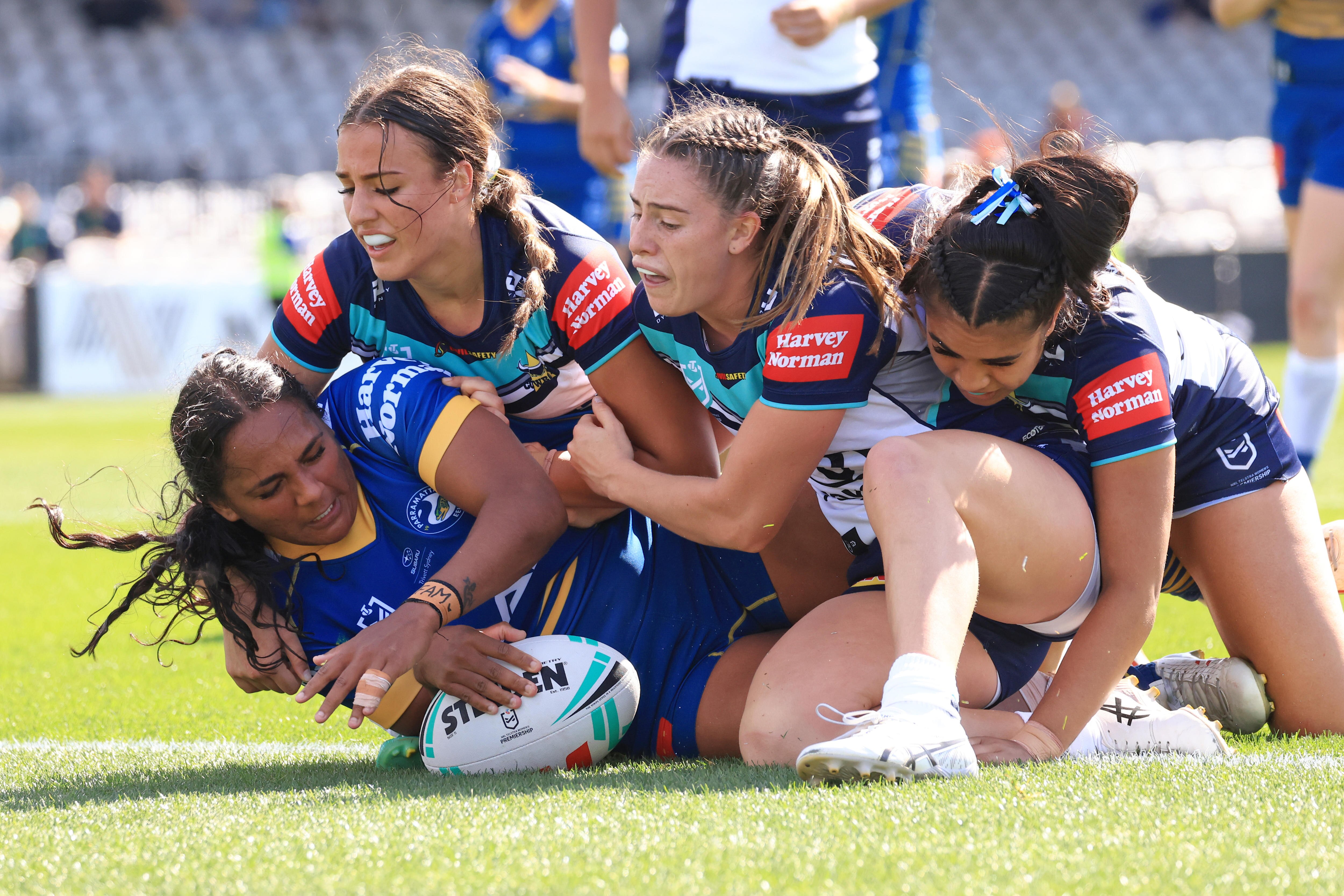 A Parramatta NRLW player scores a try as three North Queensland opponents attempt to make a tackle.