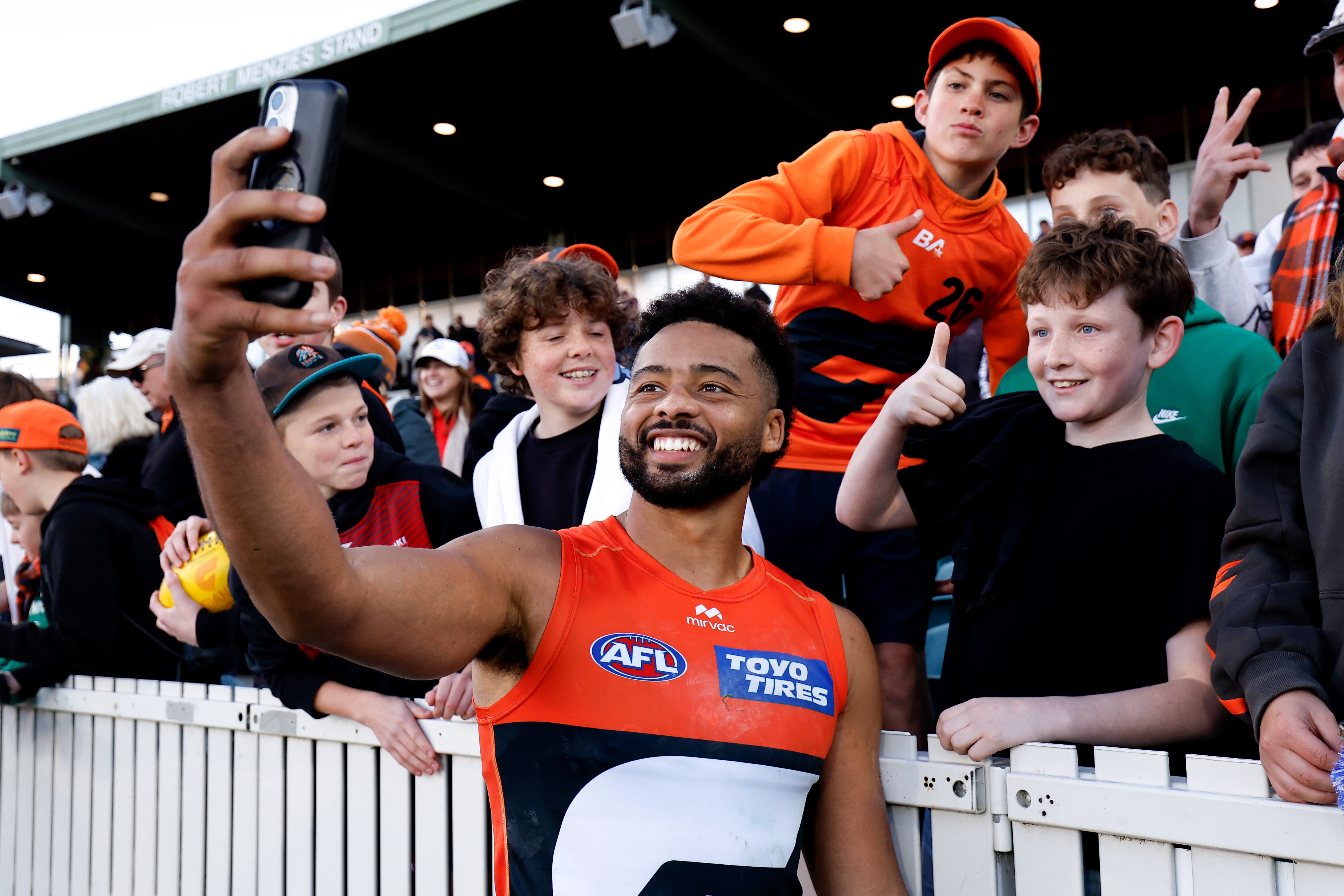A GWS AFL player smiles as he takes a selfie with a young fan after a win.