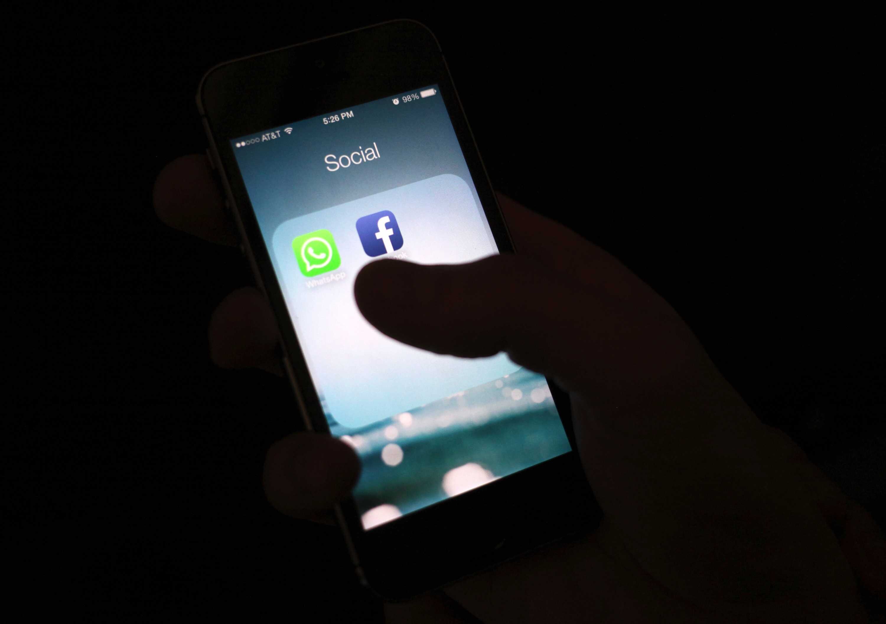 A phone shows up WhatsApp and Facebook apps against a black background.