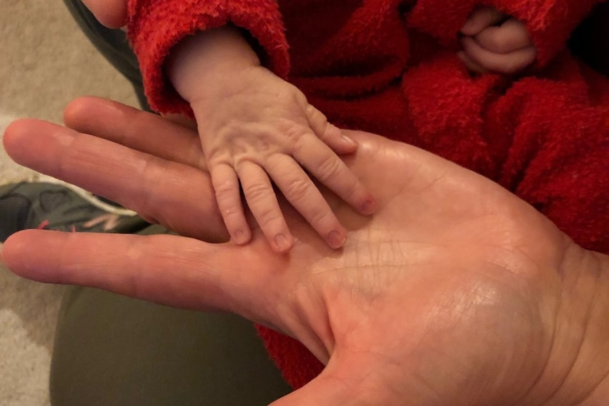 Tiny newborn hand sits on top of adult hand