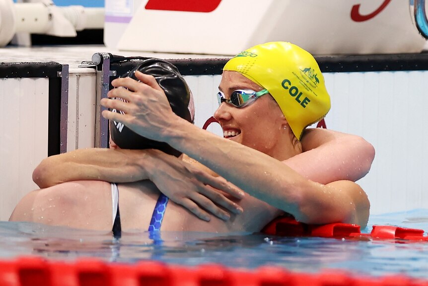 Ellie Cole, wearing her gold Australian swimming cap, hugs competitors in the pool at the Tokyo Paralympics.