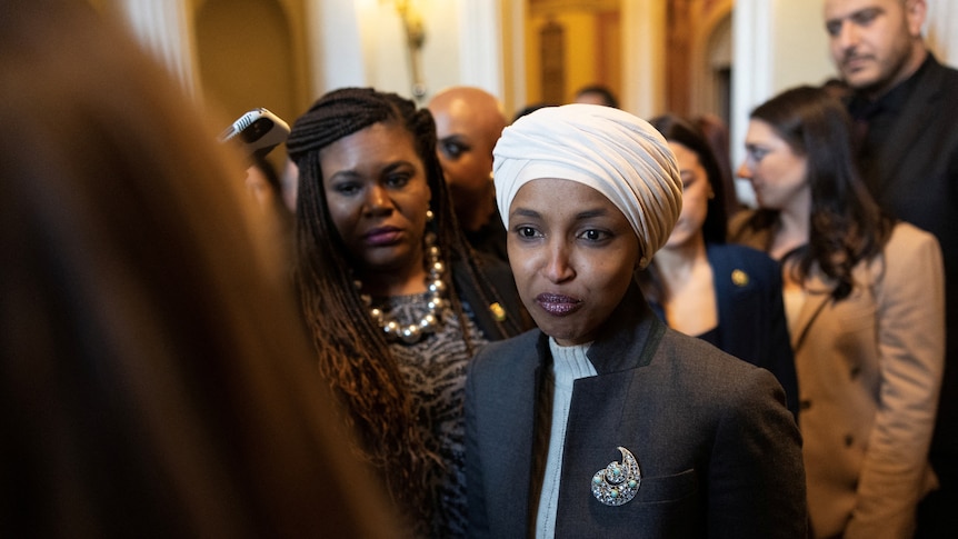 Ilhan Omar stands with her staff in a hallway. 