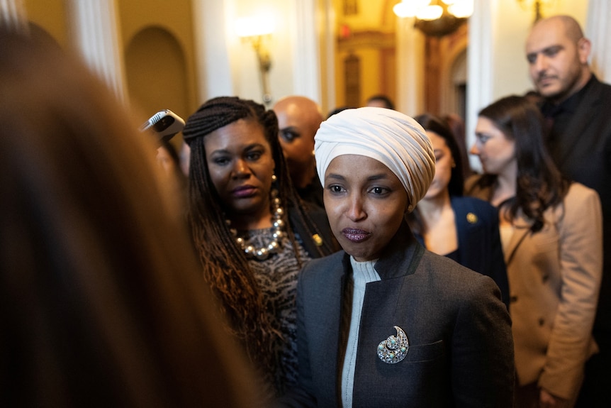 Ilhan Omar stands with her staff in a hallway. 