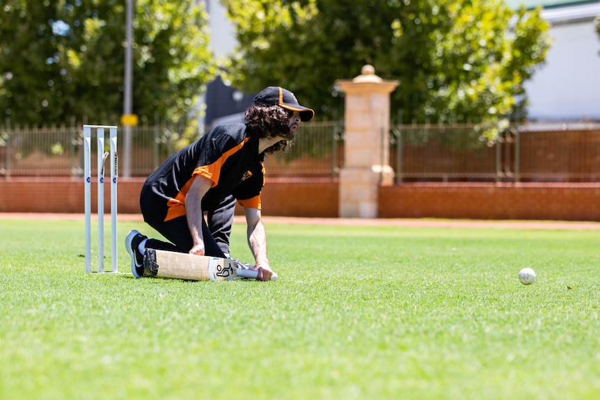 A man kneels to the ground to play blind cricket.