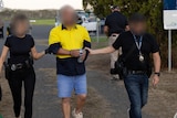 A man in a high-vis work shirt being led in handcuffs
