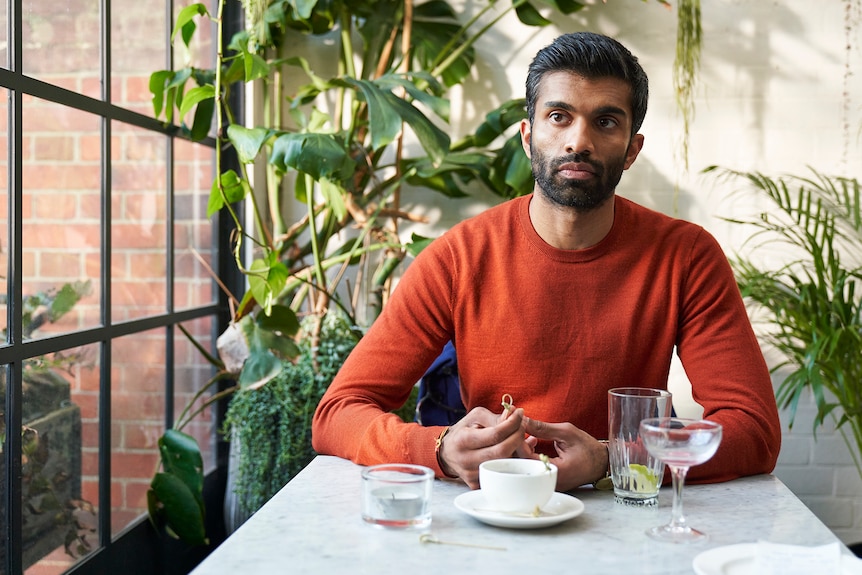 Nikesh Patel sitting at a cafe at lunch looking concerned, fidgeting with a skewer, in Starstruck