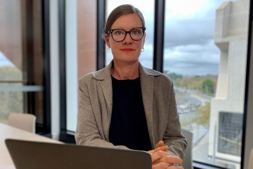 Kate Noble sits at a desk with a laptop in an office building.