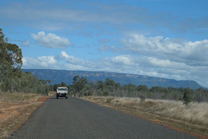 A ute drives on a bituman road with the Blackdown Tablelands loom
