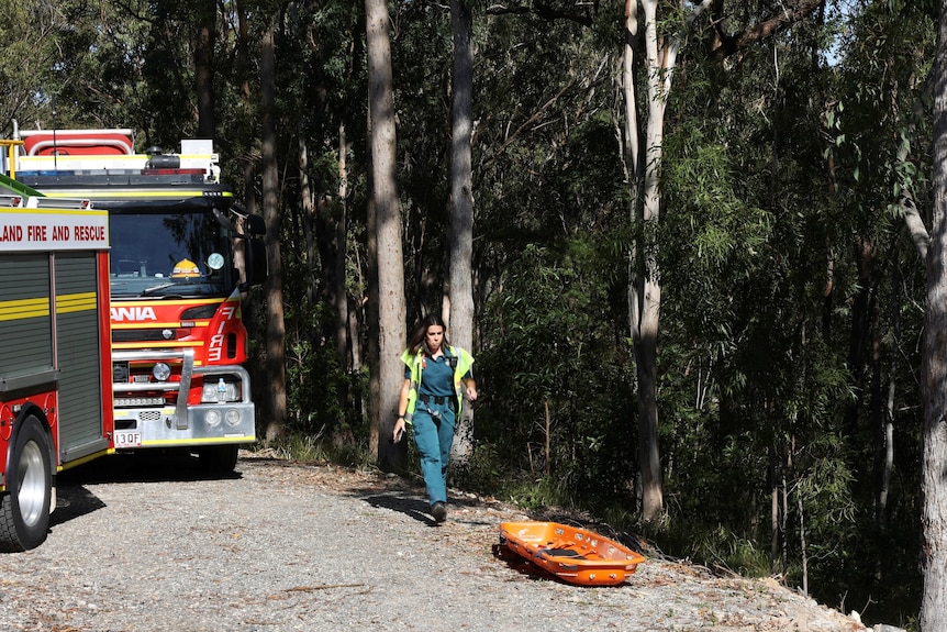 An ambulance officer walks by an embankment with an orange rescue stretcher on the ground.