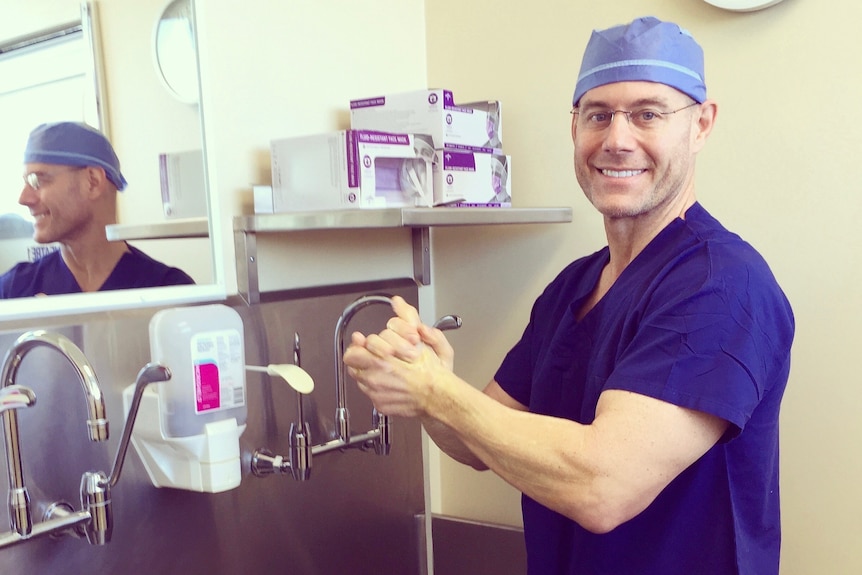 A doctor washes his hands while wearing scrubs.