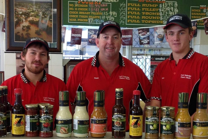 Three butchers in red shirts poses for a photo.