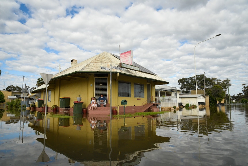 A family sits on the front steps of a home surrounded by floodwaters.