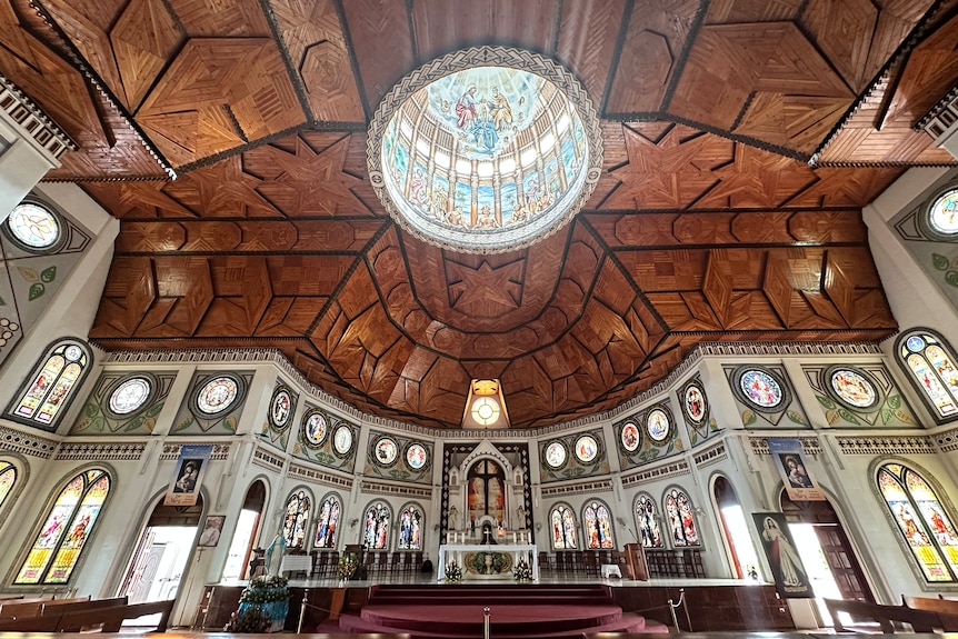 The wooden ceiling of Samoa's Immaculate Conception Cathedral, with the inside of the dome and stain glass windows illuminated.
