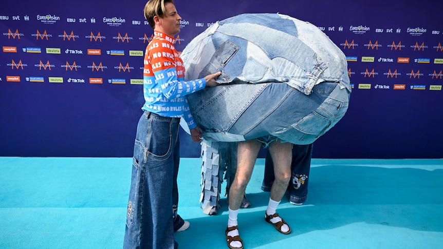 Two people inside a denim-covered egg-like shell one wearing shorts, socks and sandals, the other in jeans