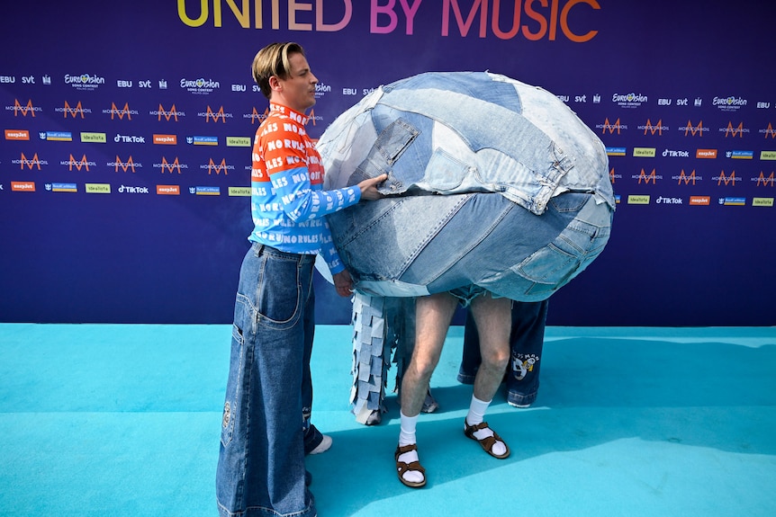 Two people inside a denim-covered egg-like shell one wearing shorts, socks and sandals, the other in jeans