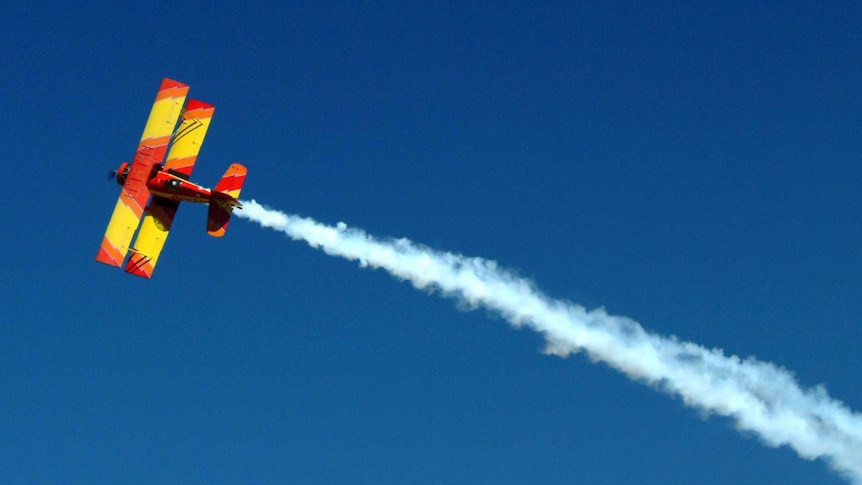 A small red and yellow plane leaves a trail of white smoke in the sky.