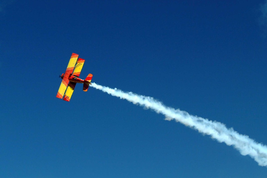 A small red and yellow plane leaves a trail of white smoke in the sky.