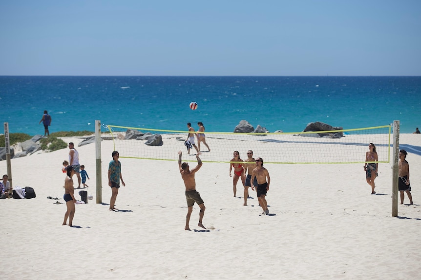 People in swimsuits play beach volleyball on a sunny day with blue sea behind them
