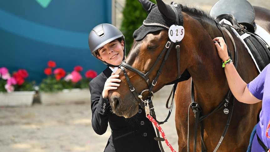 A teenager stands beside a horse wearing horse riding gear