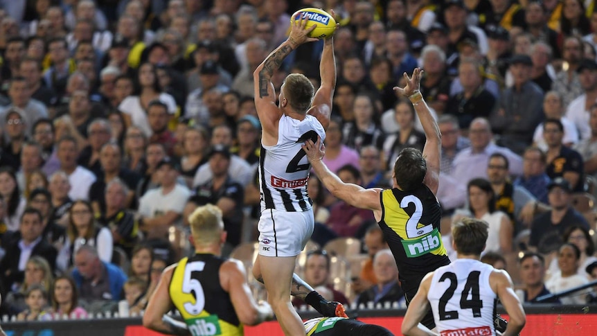 AFL player soars to take a big mark as teammates and opponents look on.