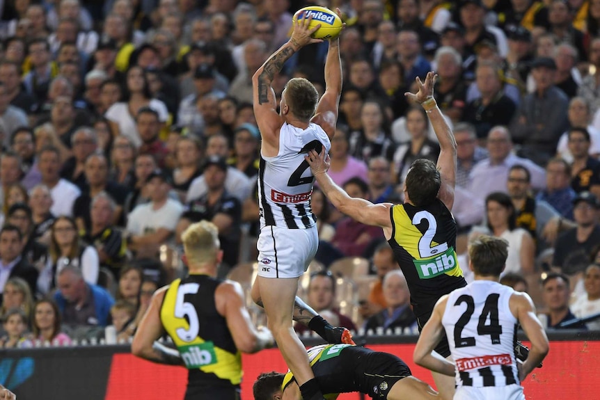 AFL player soars to take a big mark as teammates and opponents look on.
