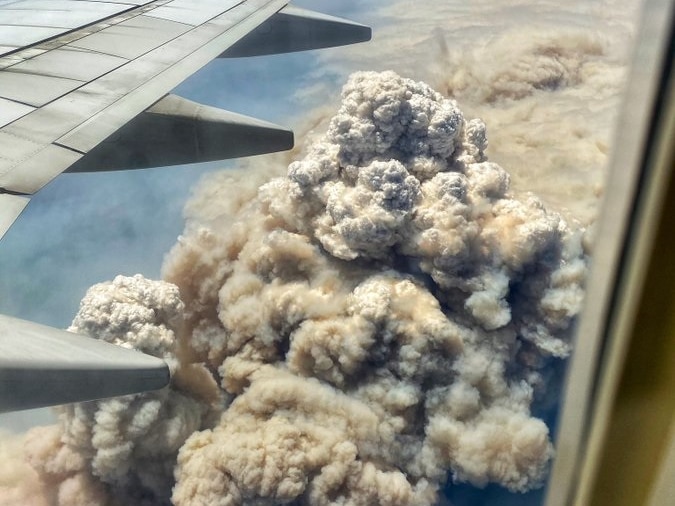 The wing of a plane, with a large plume of smoke below it.