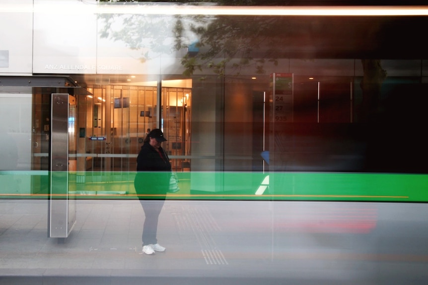 An unidentifiable woman wearing a baseball cap while standing at a bus stop