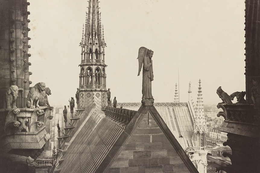 A black and white image shows the roof of the Notre Dame cathedral adorned with gargoyles and angel statues.